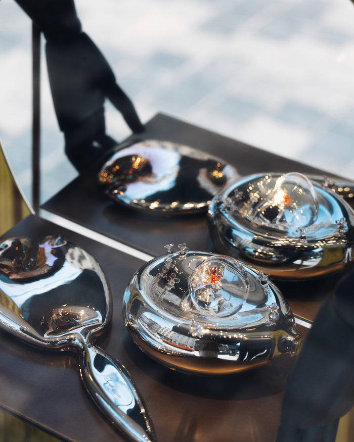 Artistic renditions of a mirror and dish made of glass placed on a black surface, in front of a mirror. 