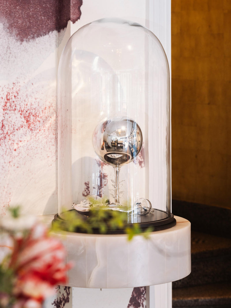 Decorative object under a glass dome on a marble surface with a circular staircase on the background