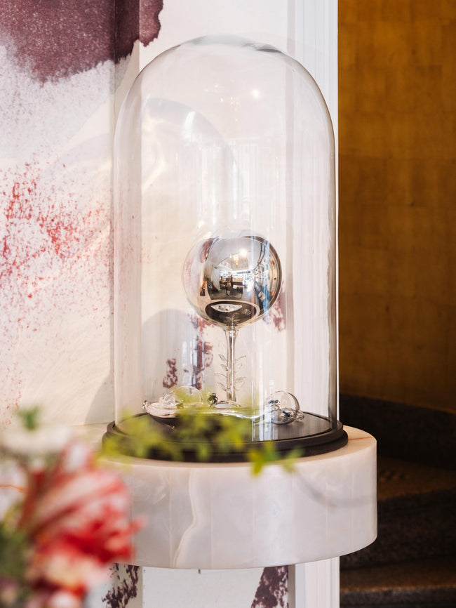 Decorative object under a glass dome on a marble surface with a circular staircase on the background