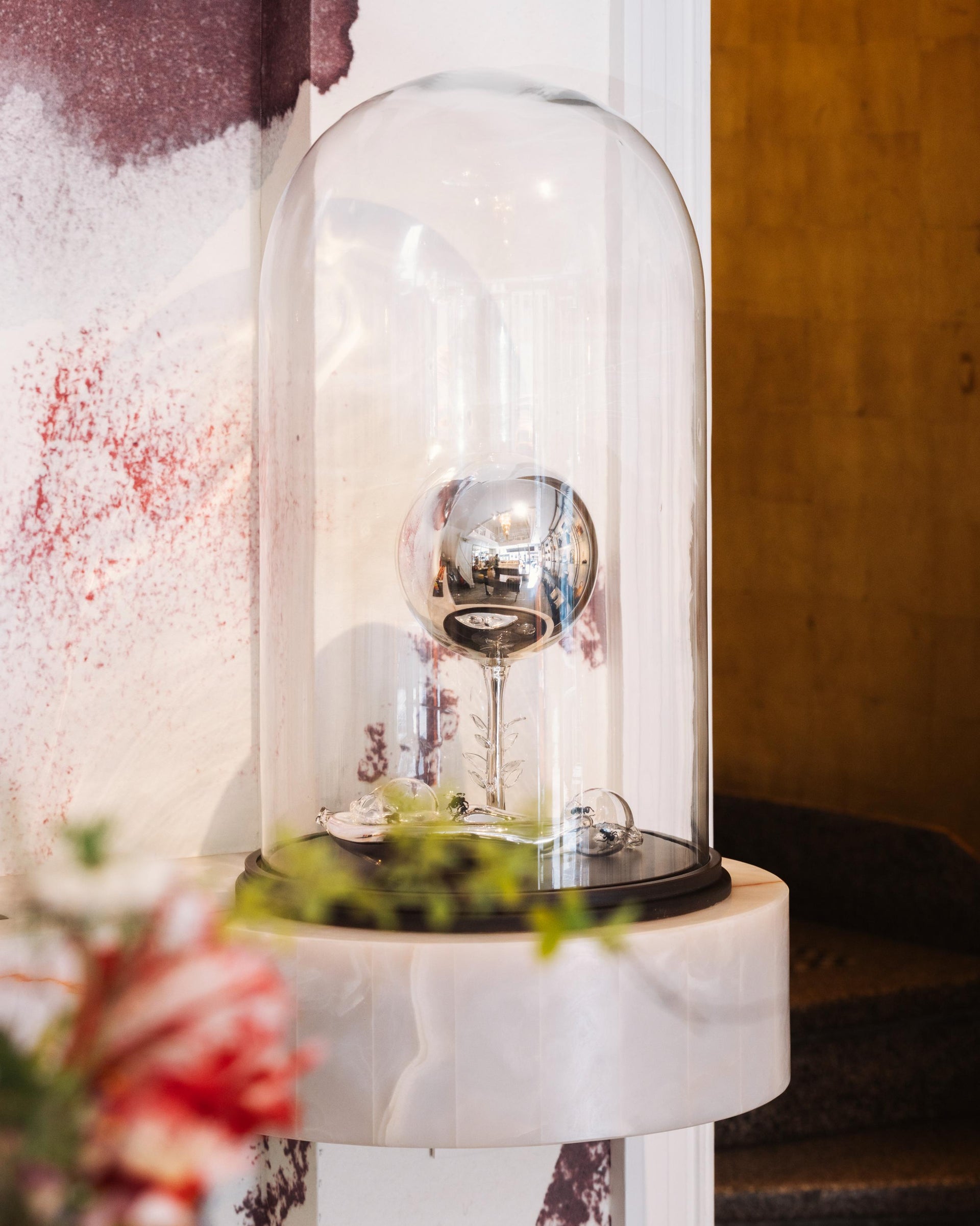 Decorative object under a glass dome on a marble surface with a circular staircase on the background