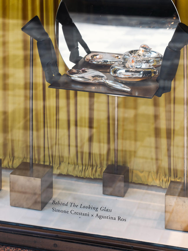 Metallic sculpture with glass panels on a stand, featuring 'Behind The Looking Glass' by Simone Crestani x Agustina Ros.