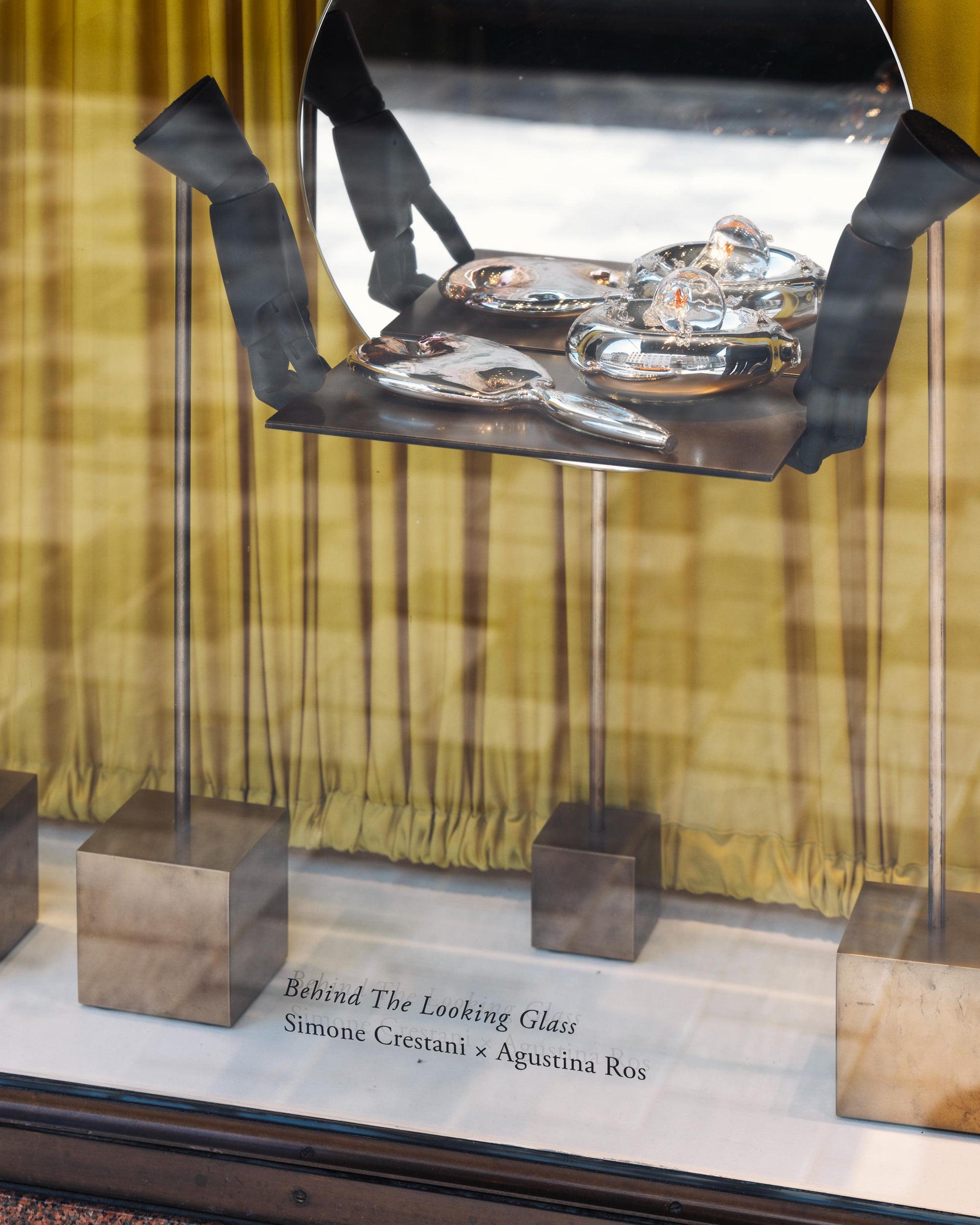 Metallic sculpture with glass panels on a stand, featuring 'Behind The Looking Glass' by Simone Crestani x Agustina Ros.