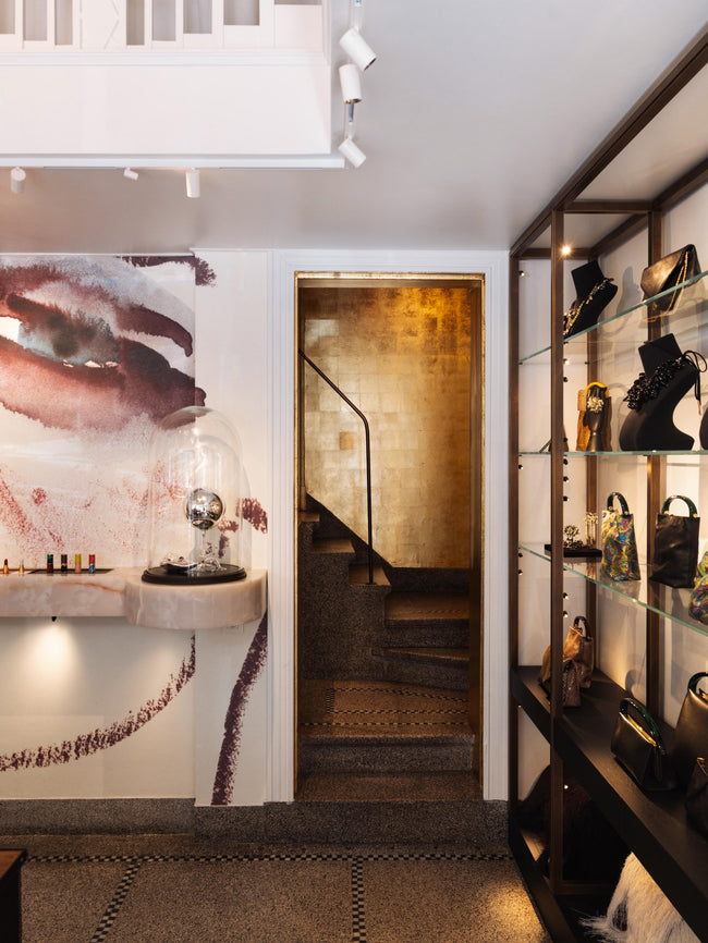 Modern interior with a staircase, wall art, and shelves showcasing handbags and jewellery.