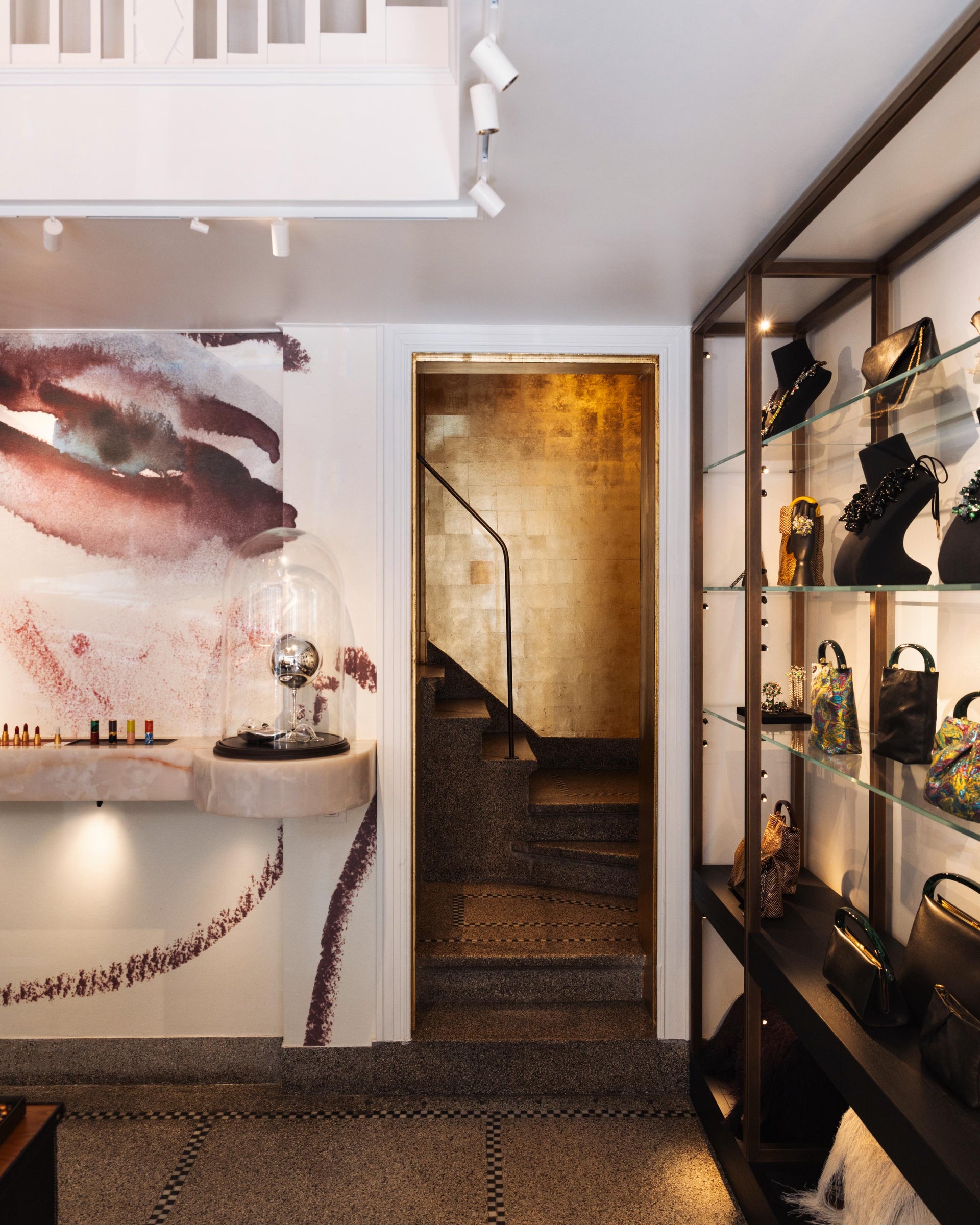 Modern interior with a staircase, wall art, and shelves showcasing handbags and jewellery.