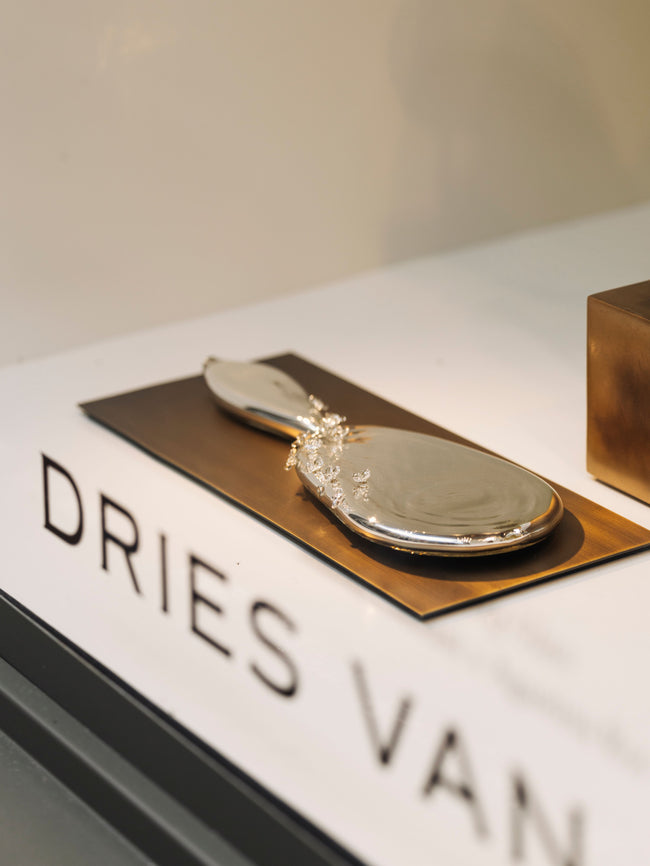 Silver oval decorative object with a handle, displayed on a bronze platform 