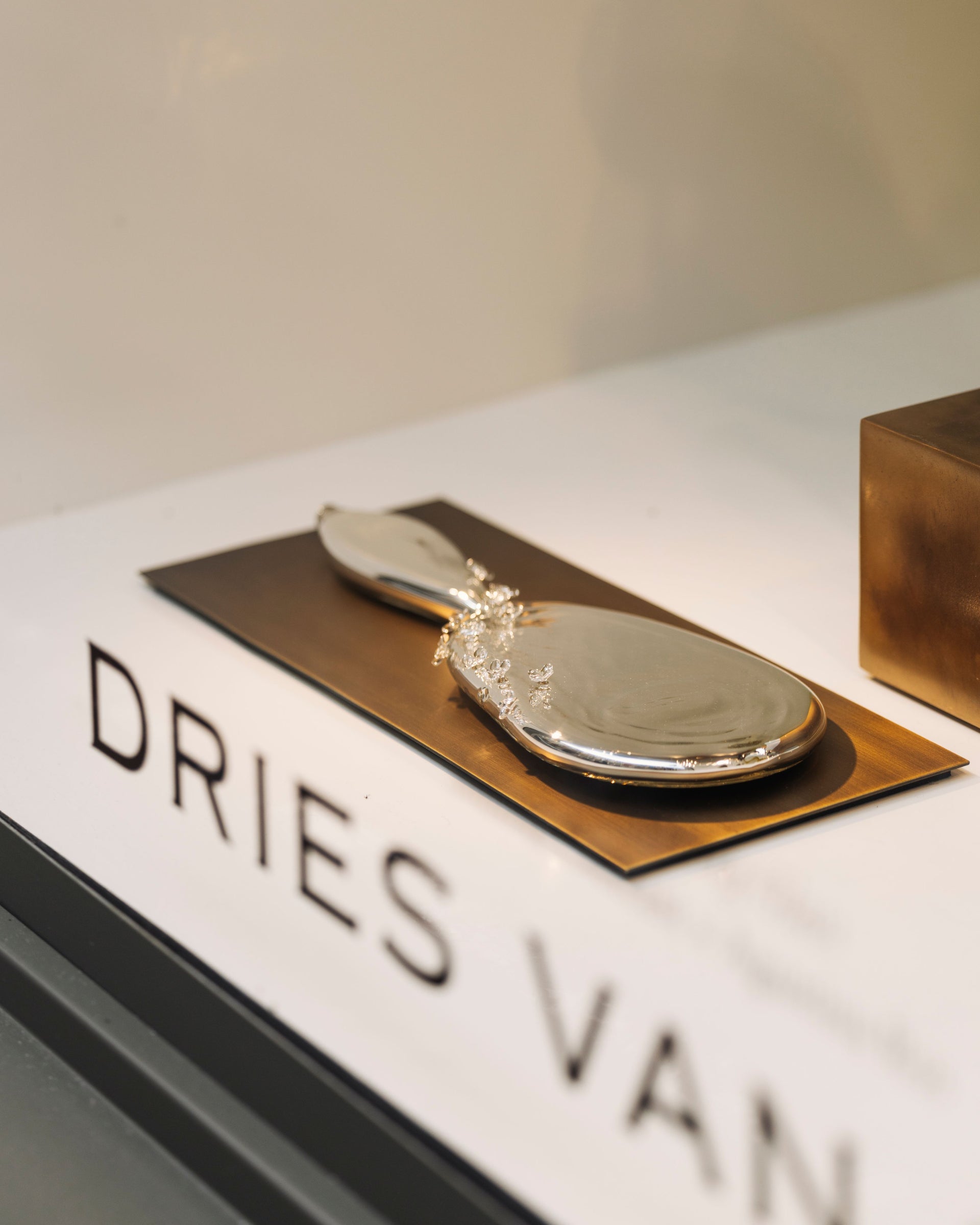 Silver oval decorative object with a handle, displayed on a bronze platform 