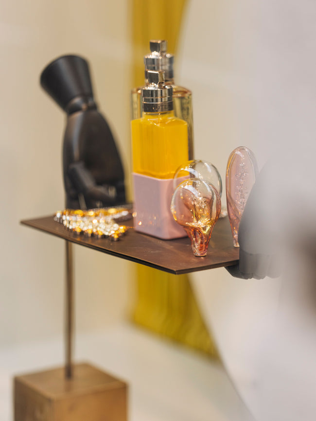 Perfume bottle displayed on a small shelf with decorative objects including glass ornaments and a black sculptural figure