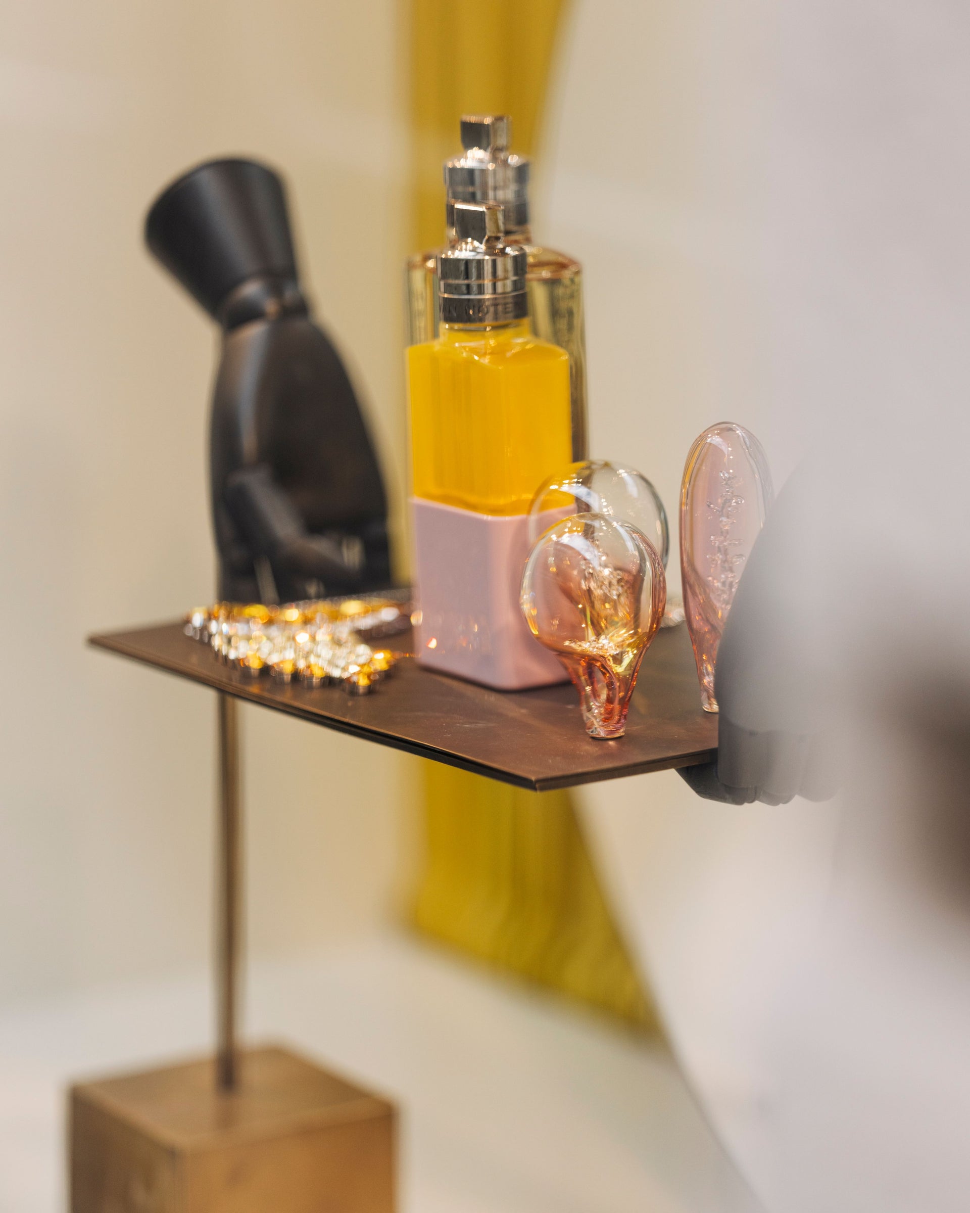 Perfume bottle displayed on a small shelf with decorative objects including glass ornaments and a black sculptural figure