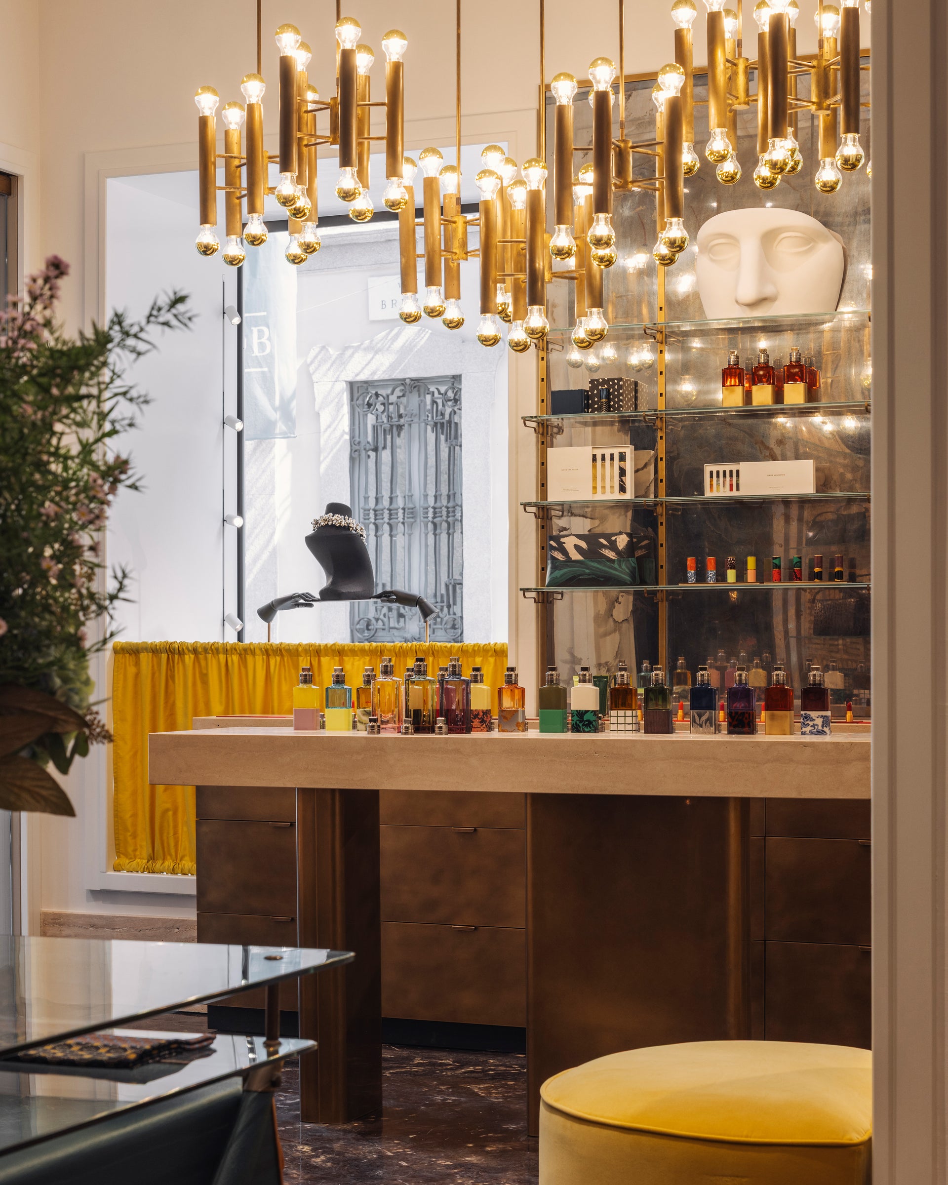 Modern interior with a bar setup featuring a chandelier, bottles on a shelf, and a yellow stool.