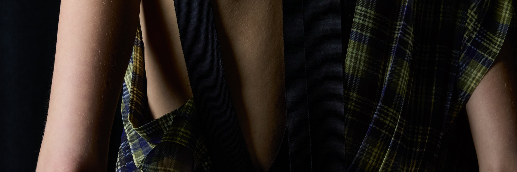 Close-up of a person wearing a dark plaid shirt, set against a dark background.