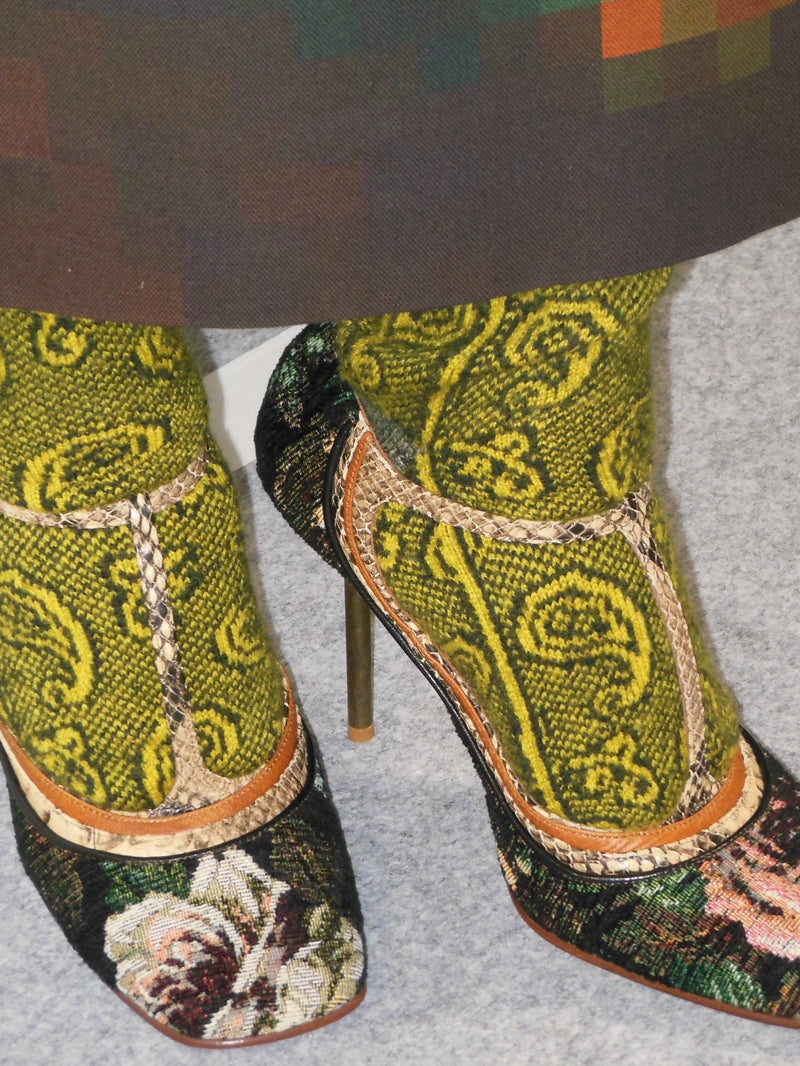 Pair of high-heeled shoes with intricate green and black patterned design on a gray background