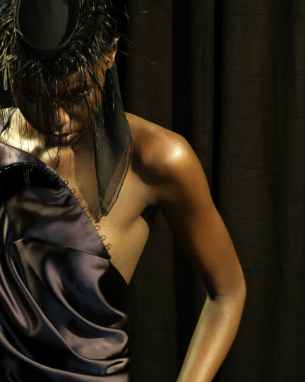 Person wearing a dark dress and a headpiece against a dark background.