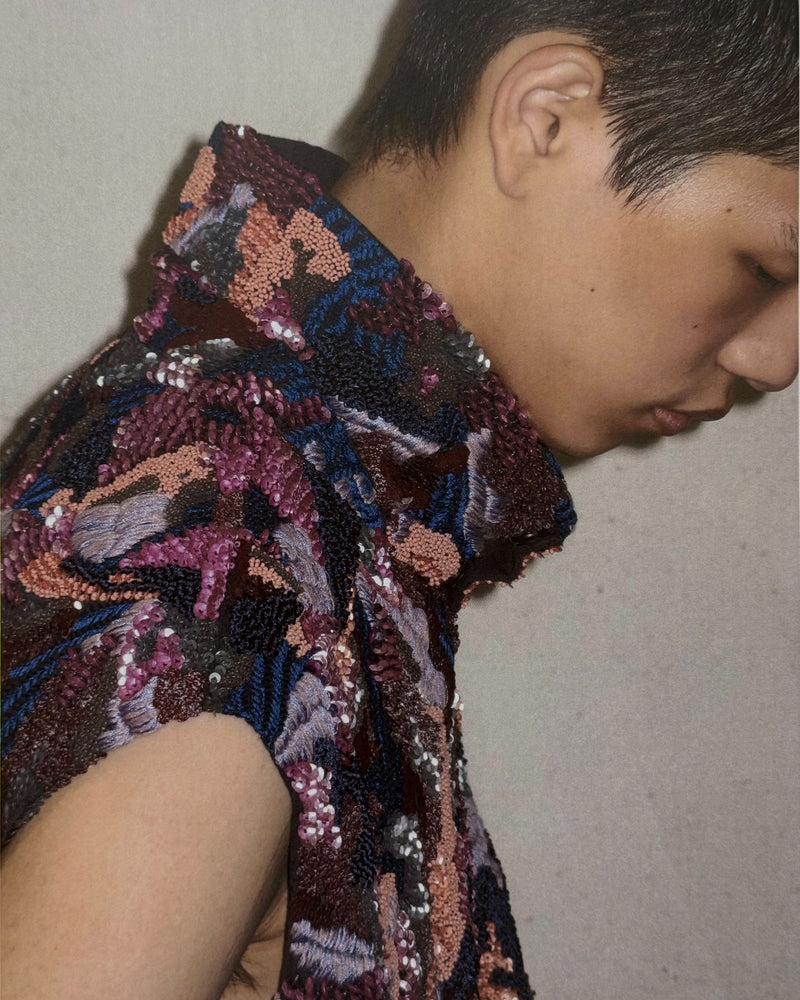 Close-up of a short haired person wearing a sequined garment with a neutral background