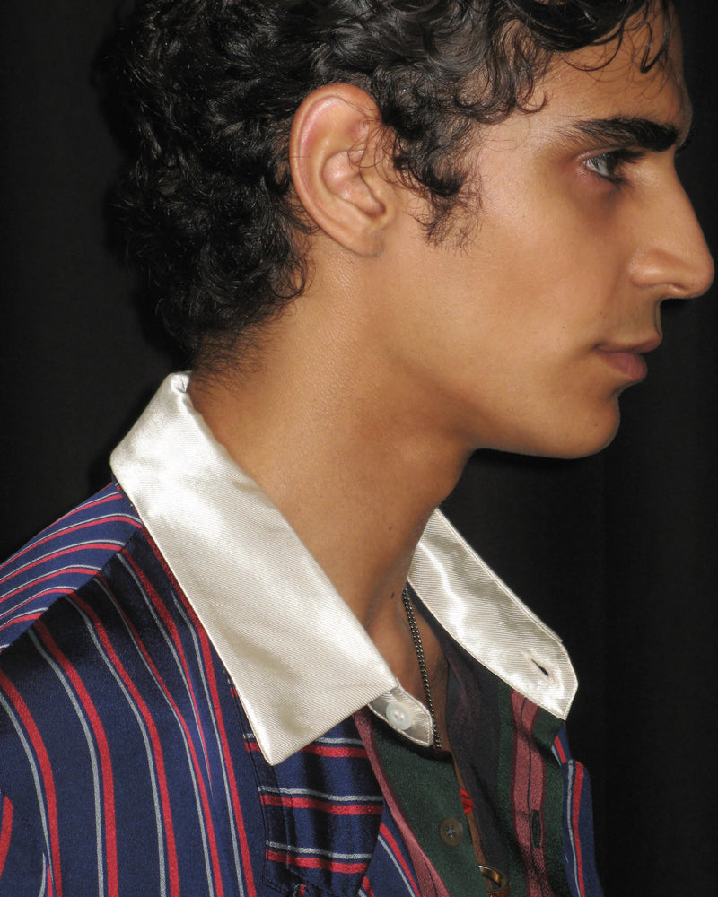 Close-up of a person wearing a striped shirt with a white collar against a dark background