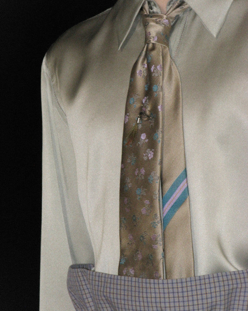 Close-up of a taupe satin shirt styled with a floral tie and high-waisted checked trousers.
