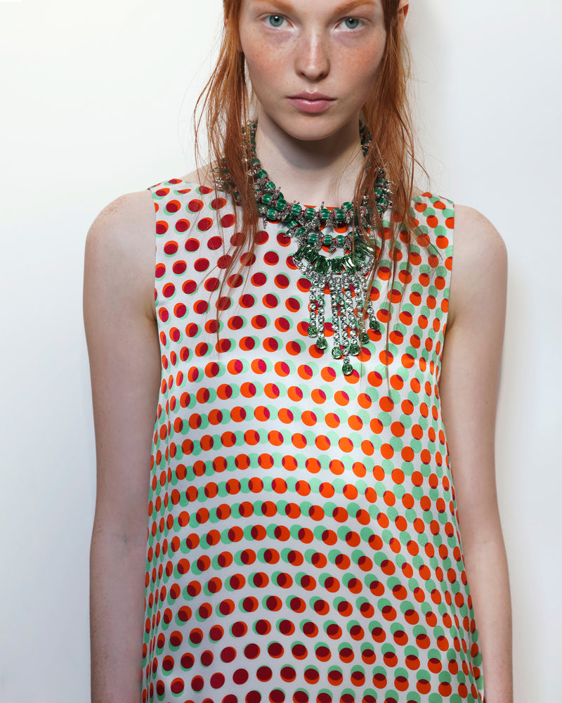 Woman wearing a polka dot dress with a green necklace on a white background