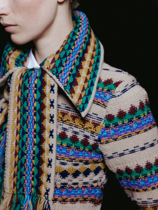 Close-up of a person wearing a patterned jacket and scarf with a dark background