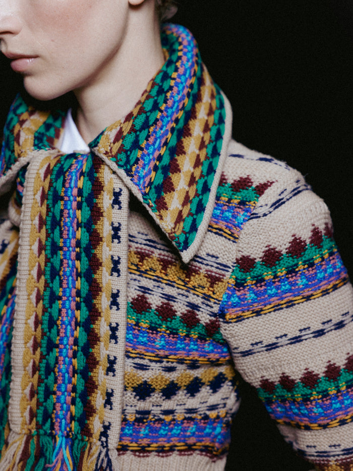 Close-up of a person wearing a patterned jacket and scarf with a dark background