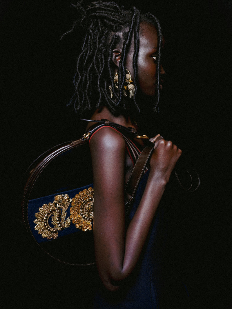 Person holding a handbag with intricate design against a dark background