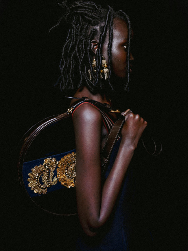Person holding a handbag with intricate design against a dark background