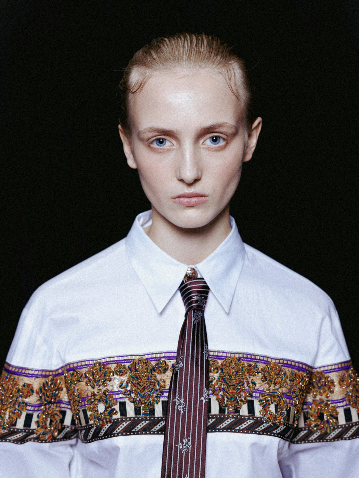 Person wearing a white shirt with a patterned tie against a black background