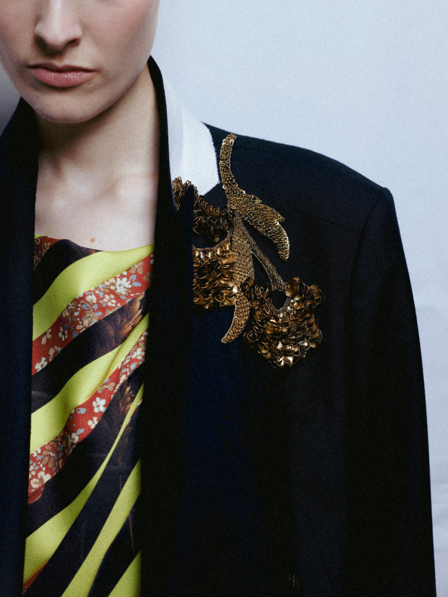 Person wearing a black blazer with a decorative brooch and a colorful striped tie.