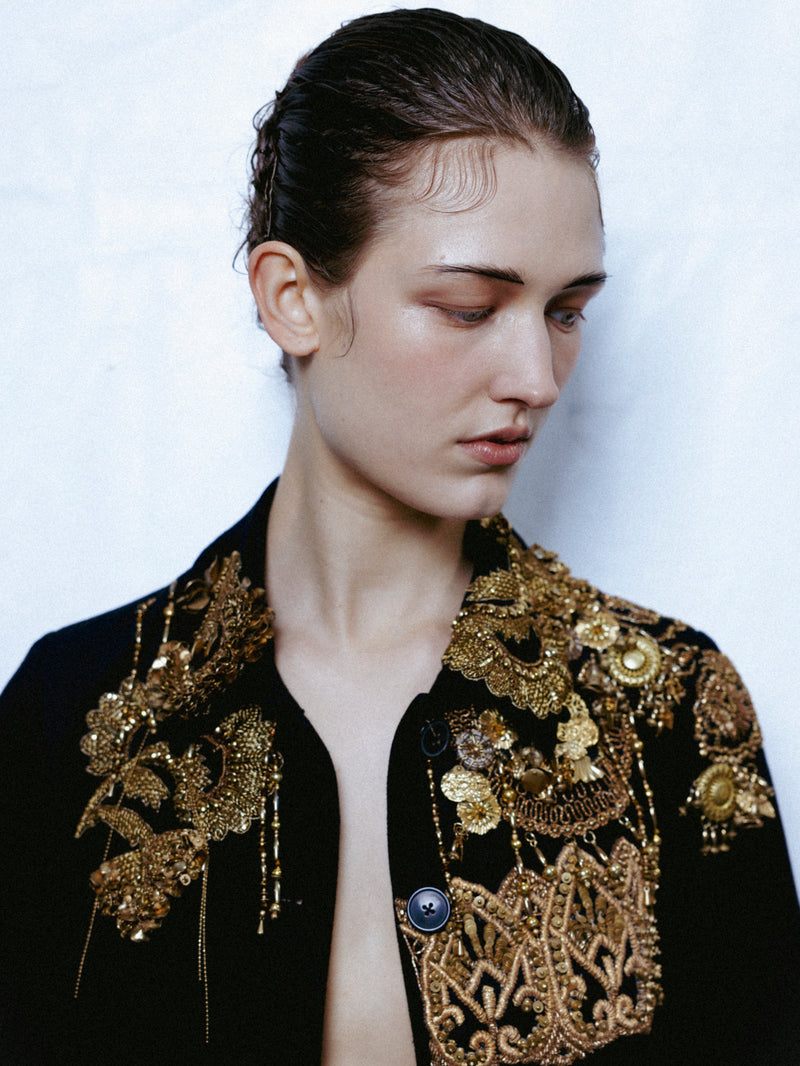 Person wearing a black and gold embroidered jacket on a white background