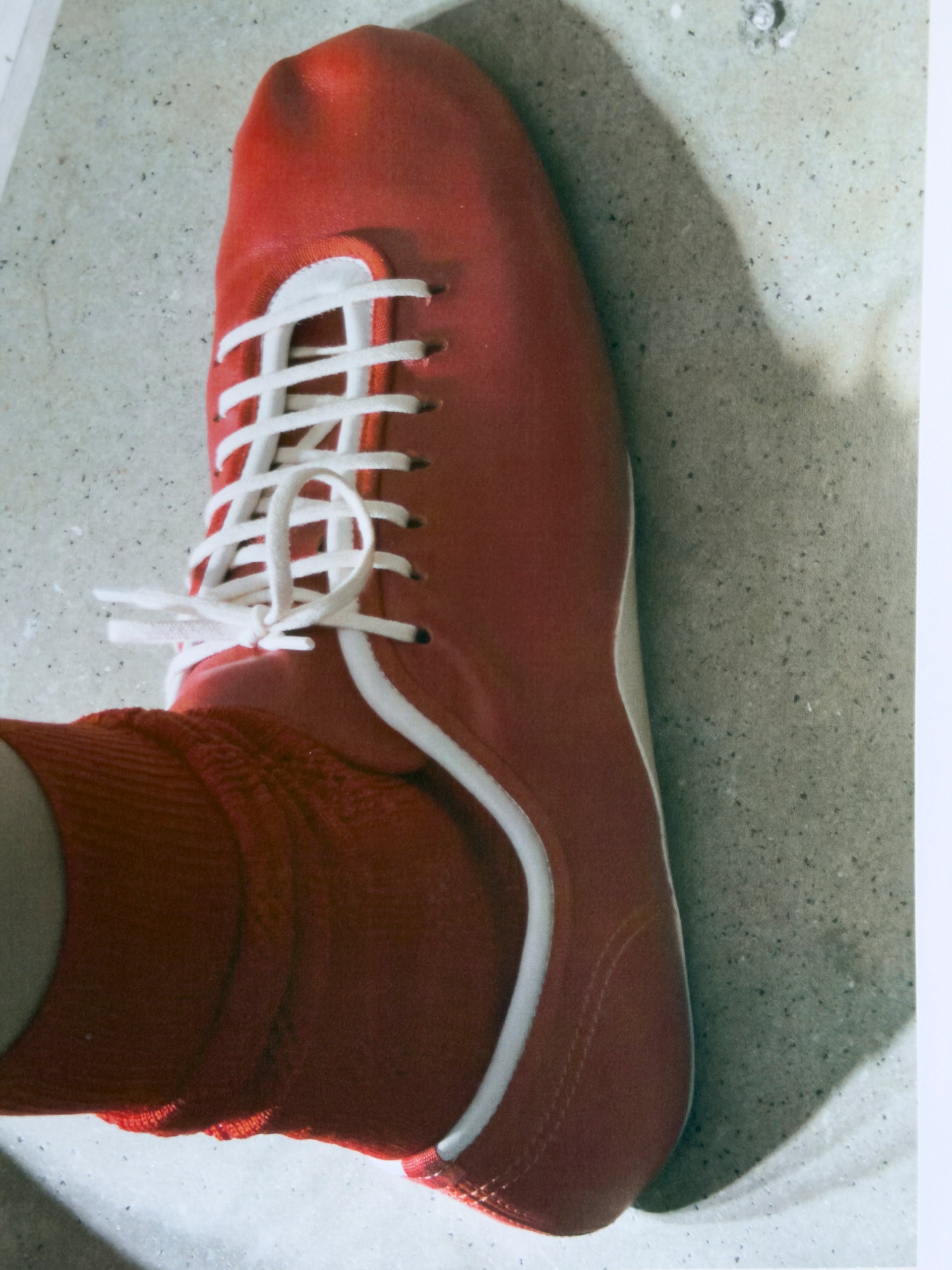 Red sneaker with white laces on a concrete floor