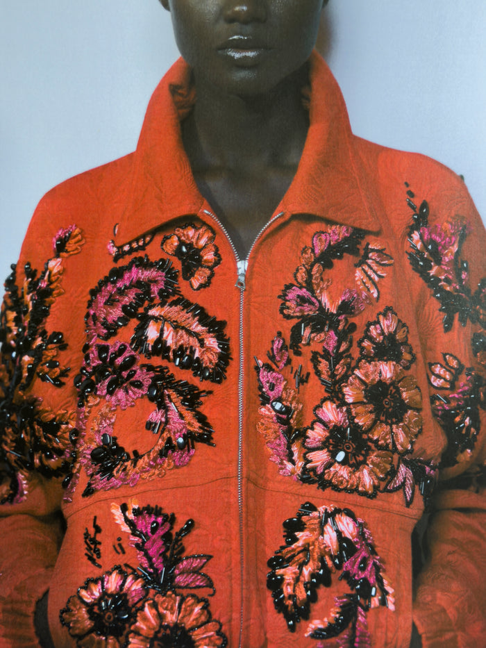 Orange jacket with floral bead embroidery on a mannequin against a plain background