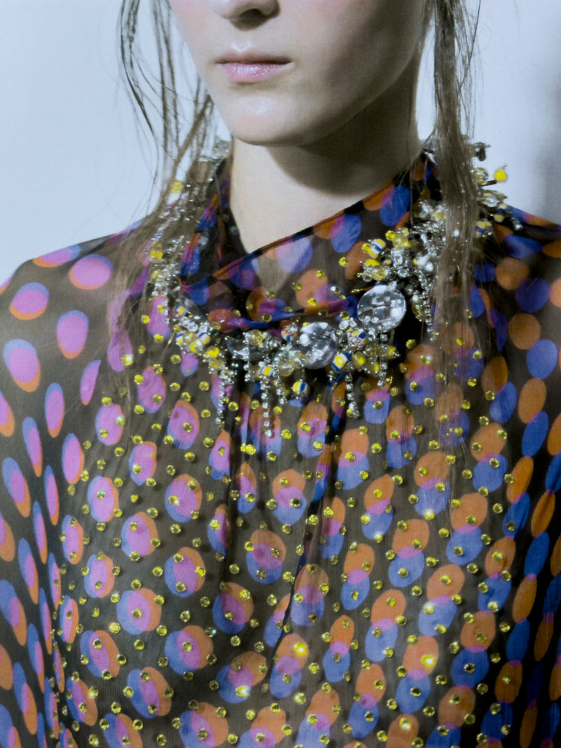 Person wearing a colorful patterned garment with a prominent necklace.
