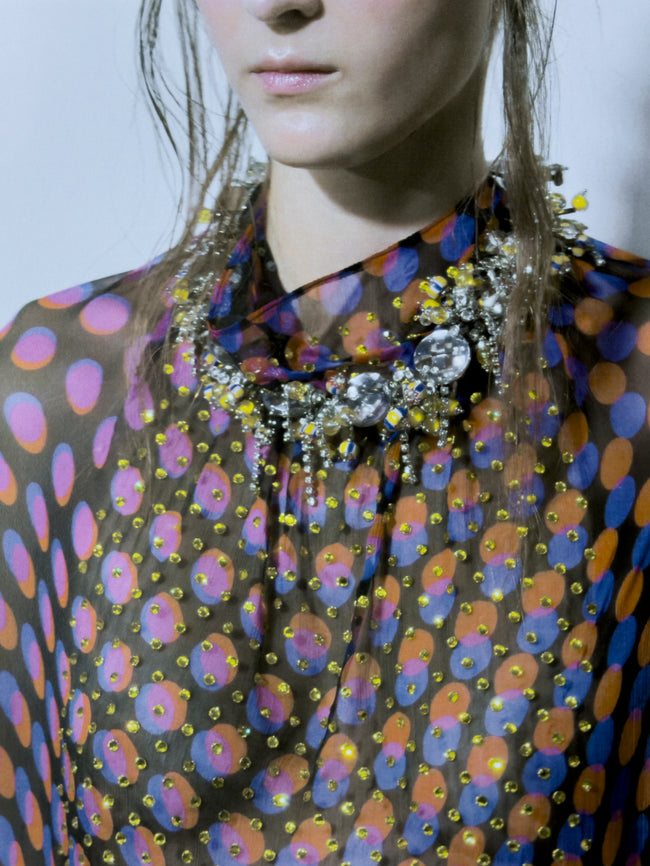 Person wearing a colorful patterned garment with a prominent necklace.