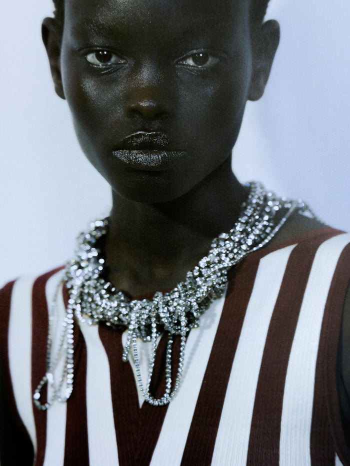 Person wearing a striped garment and a sparkling necklace against a plain background