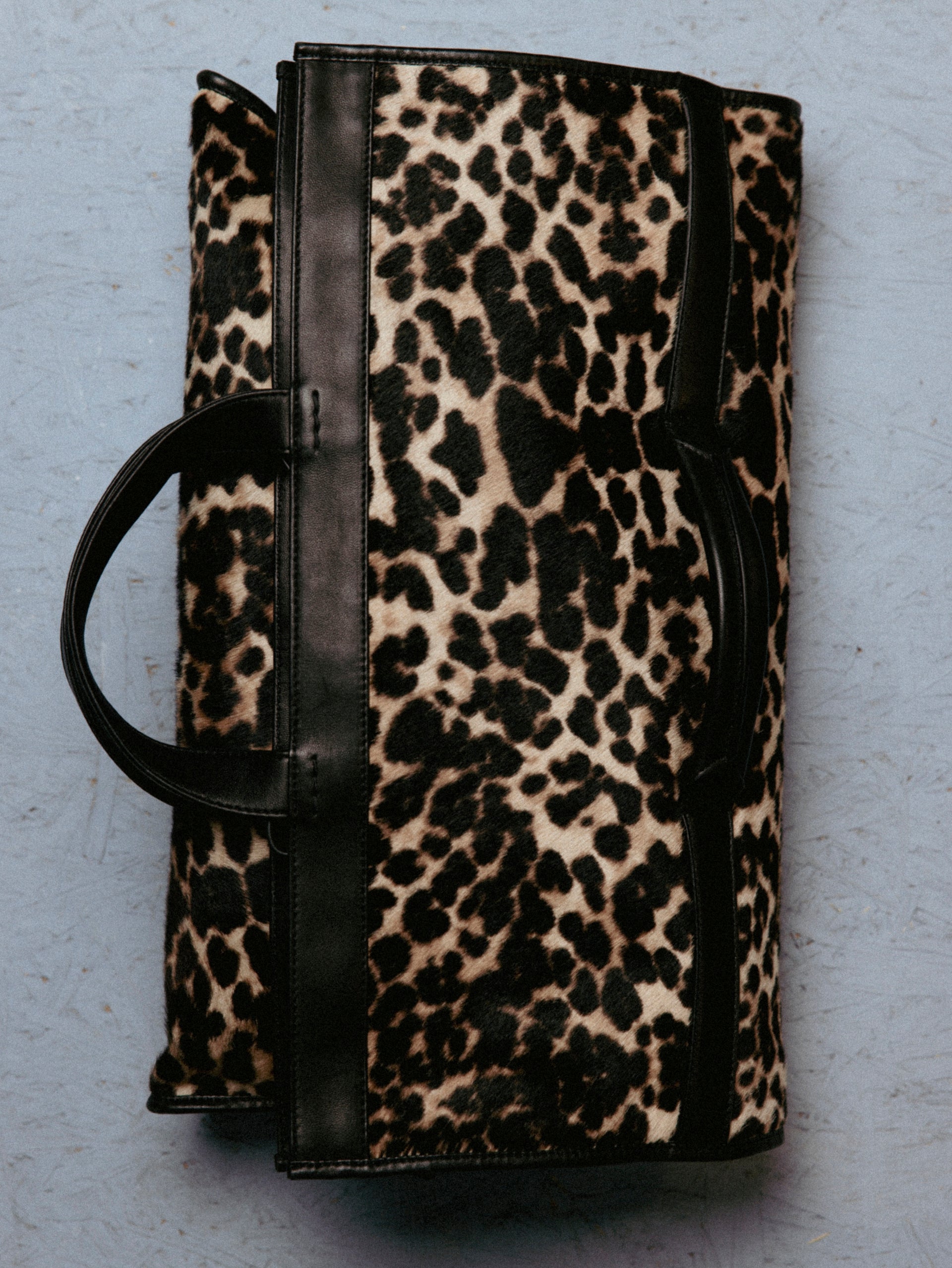 Leopard print bag with black handles on a gray background